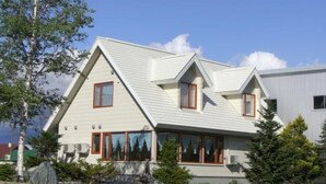 A modern two-story house with a sloped roof, large windows, and a well-maintained lawn. - Meguminoyu (Furano)