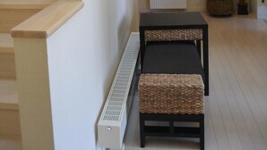 A staircase leading to a landing with a radiator, a framed artwork, and a wicker bench. - Meguminoyu (Furano)