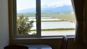 A room with a window overlooking a river and mountains. There is a table and a chair in the foreground. - Meguminoyu (Furano)