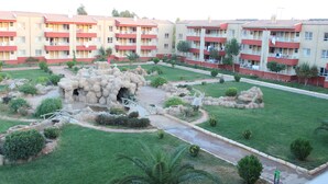 A courtyard with a rock garden, a small pond, and apartment buildings with balconies. - Karaali Kpalicalari ve Otel Tesisleri (Sanliurfa)