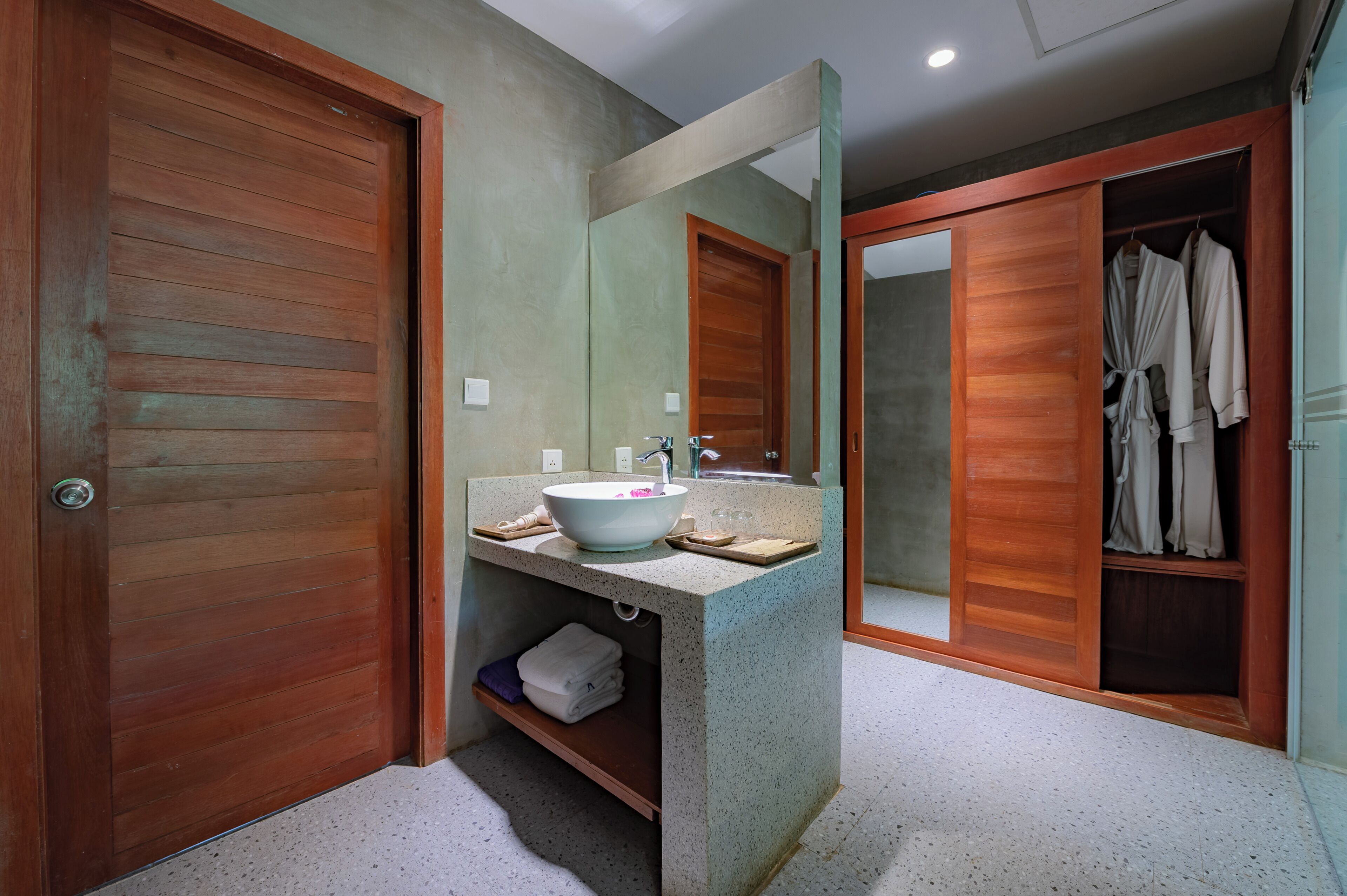 Un baño con puerta de madera, un lavabo con espejo y un perchero para batas.