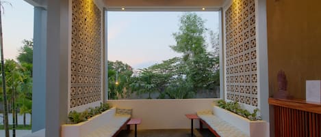 A reception area with a bench and a desk, a decorative wall, and a view of greenery outside.
