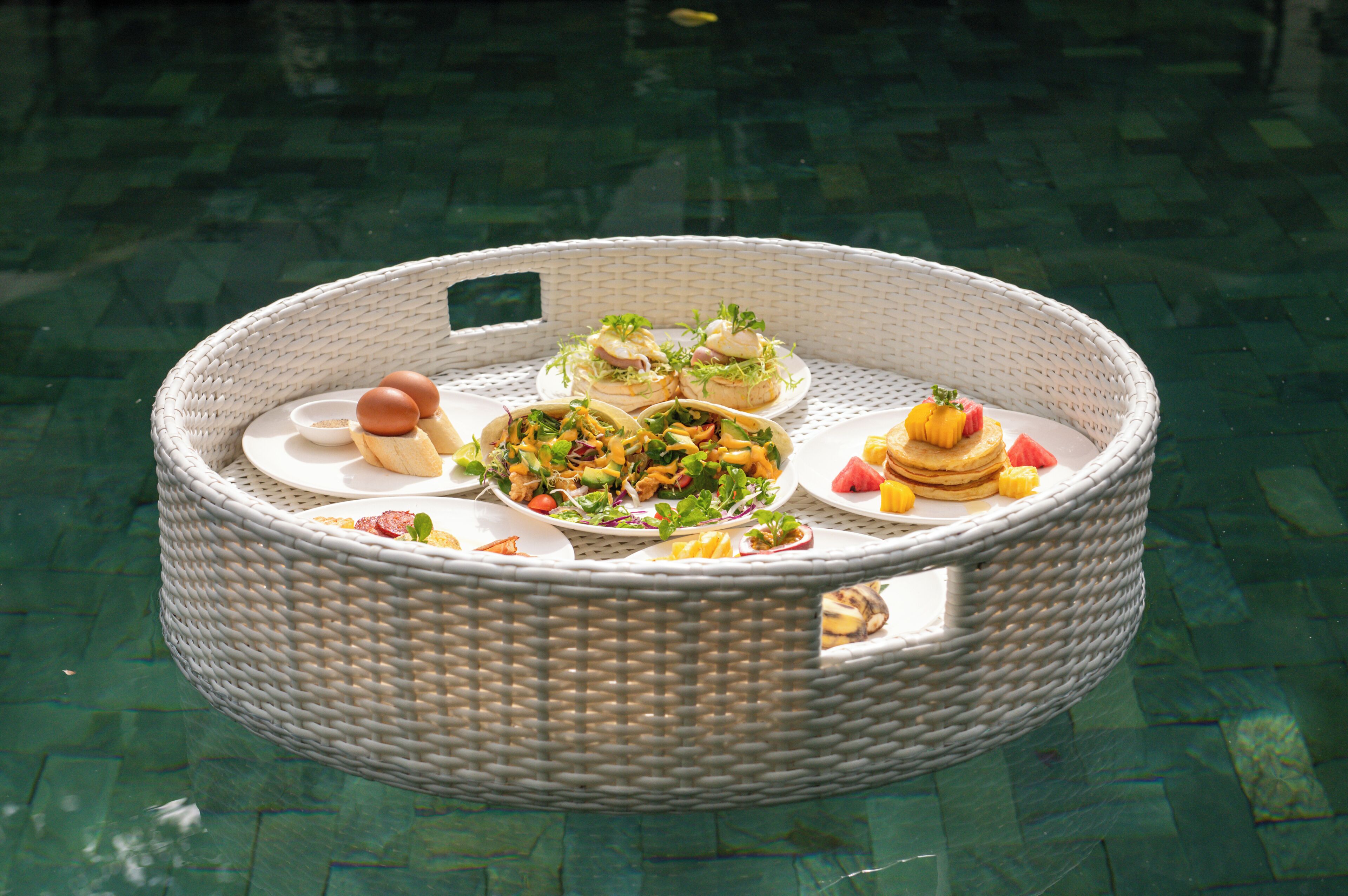 Una cesta de mimbre con diferentes alimentos sobre una mesa junto a la piscina.