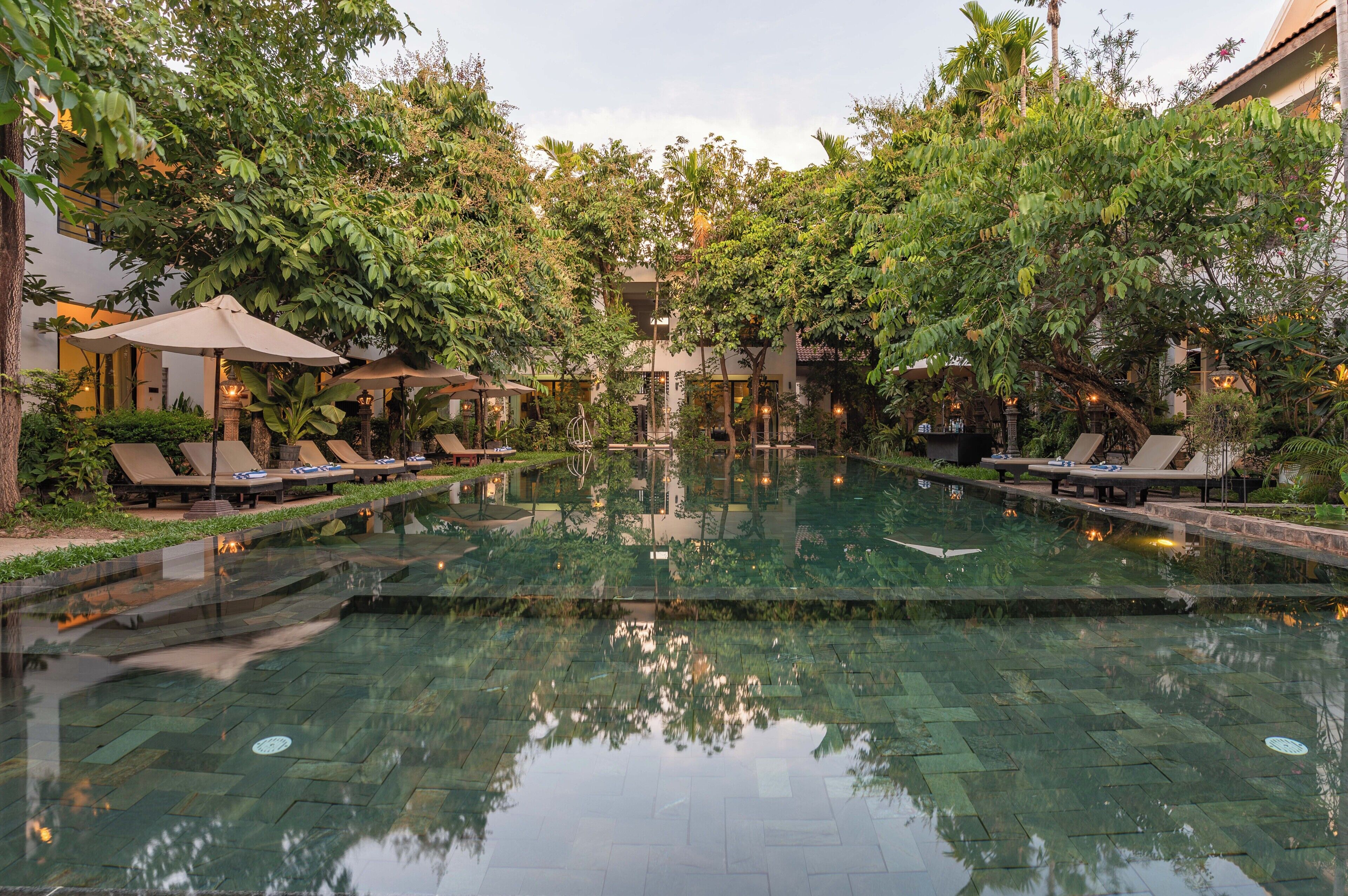 A serene indoor pool area with lounge chairs and umbrellas, surrounded by lush greenery and architectural details.