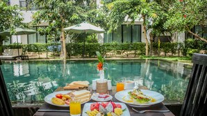 A dining table with breakfast items, a pool, and umbrellas in a hotel courtyard. - Tanei Angkor Resort and Spa (Siem Reap)