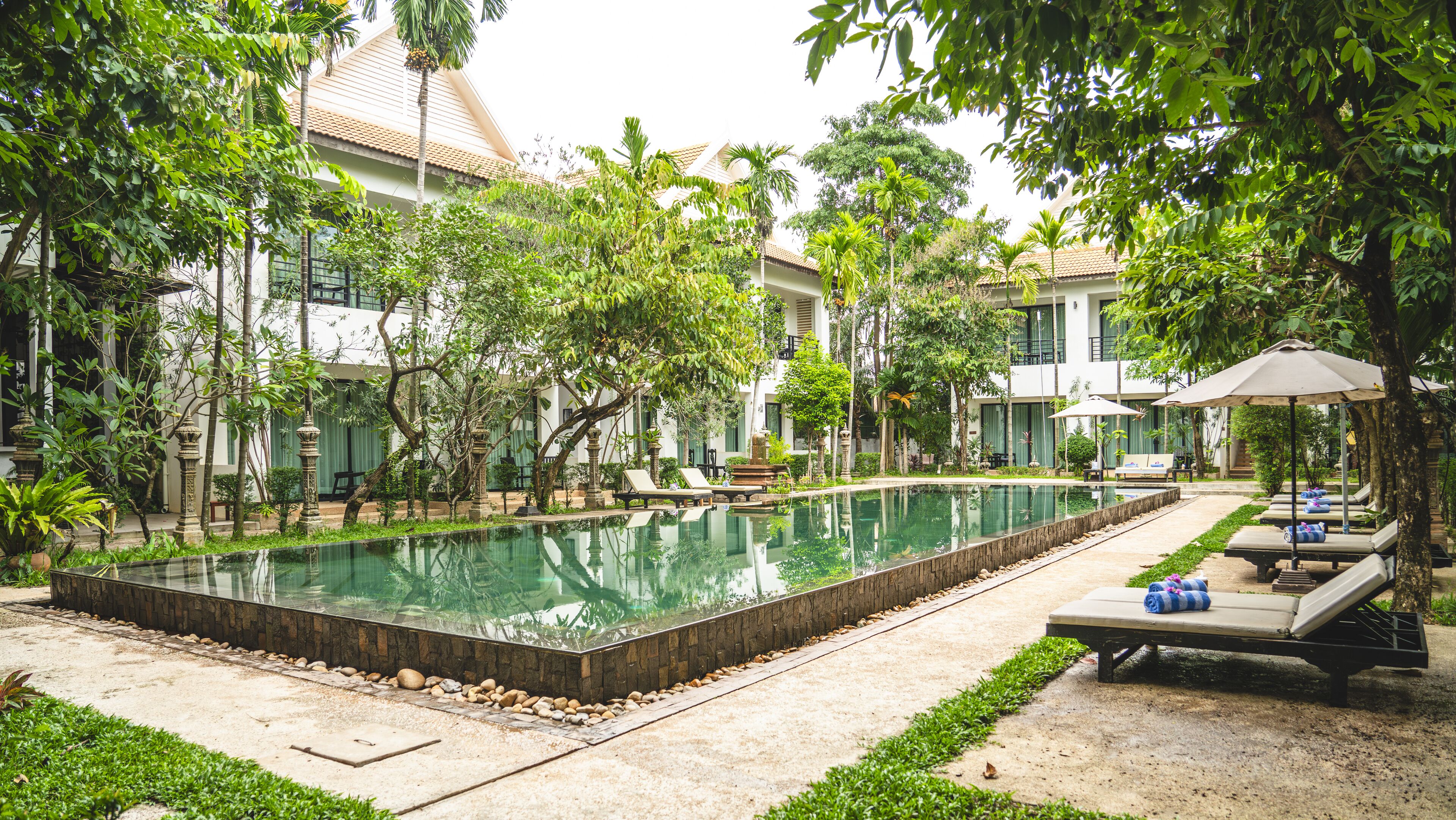 A pool area with lounge chairs and umbrellas, surrounded by trees and buildings.
