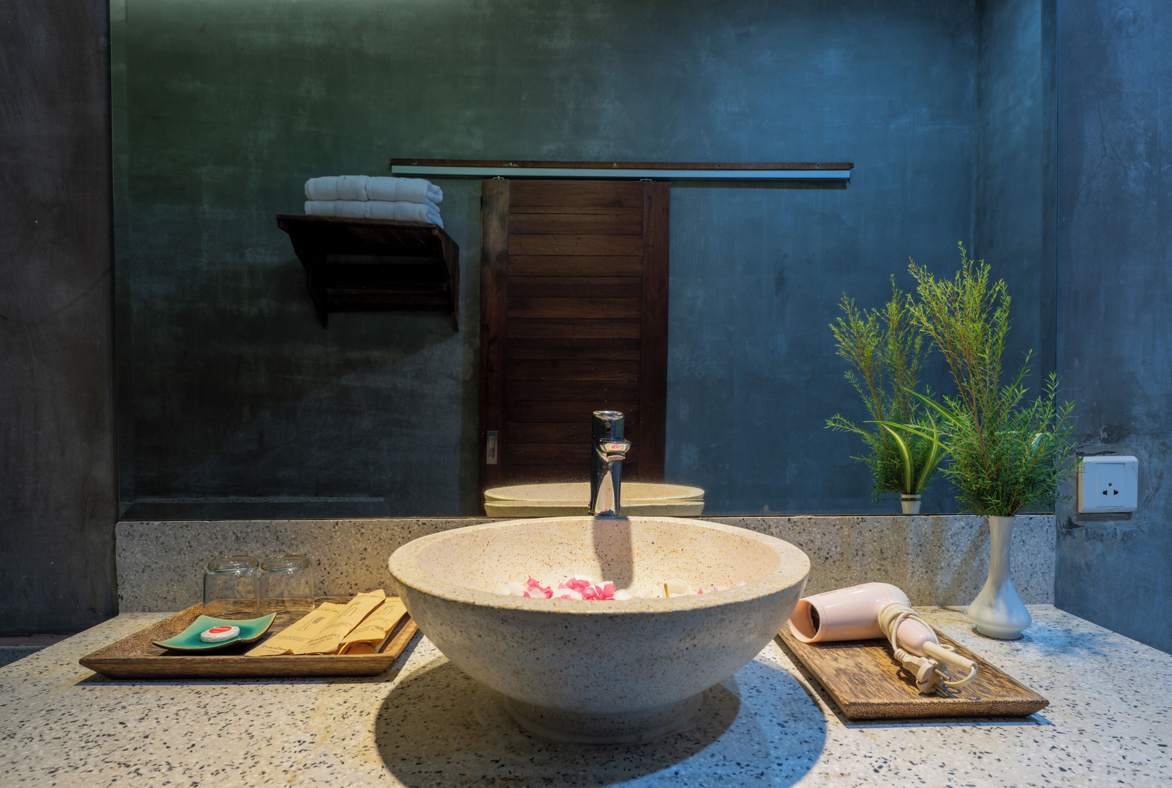 A bathroom with a large stone sink, a mirror, a towel rack, and a potted plant.