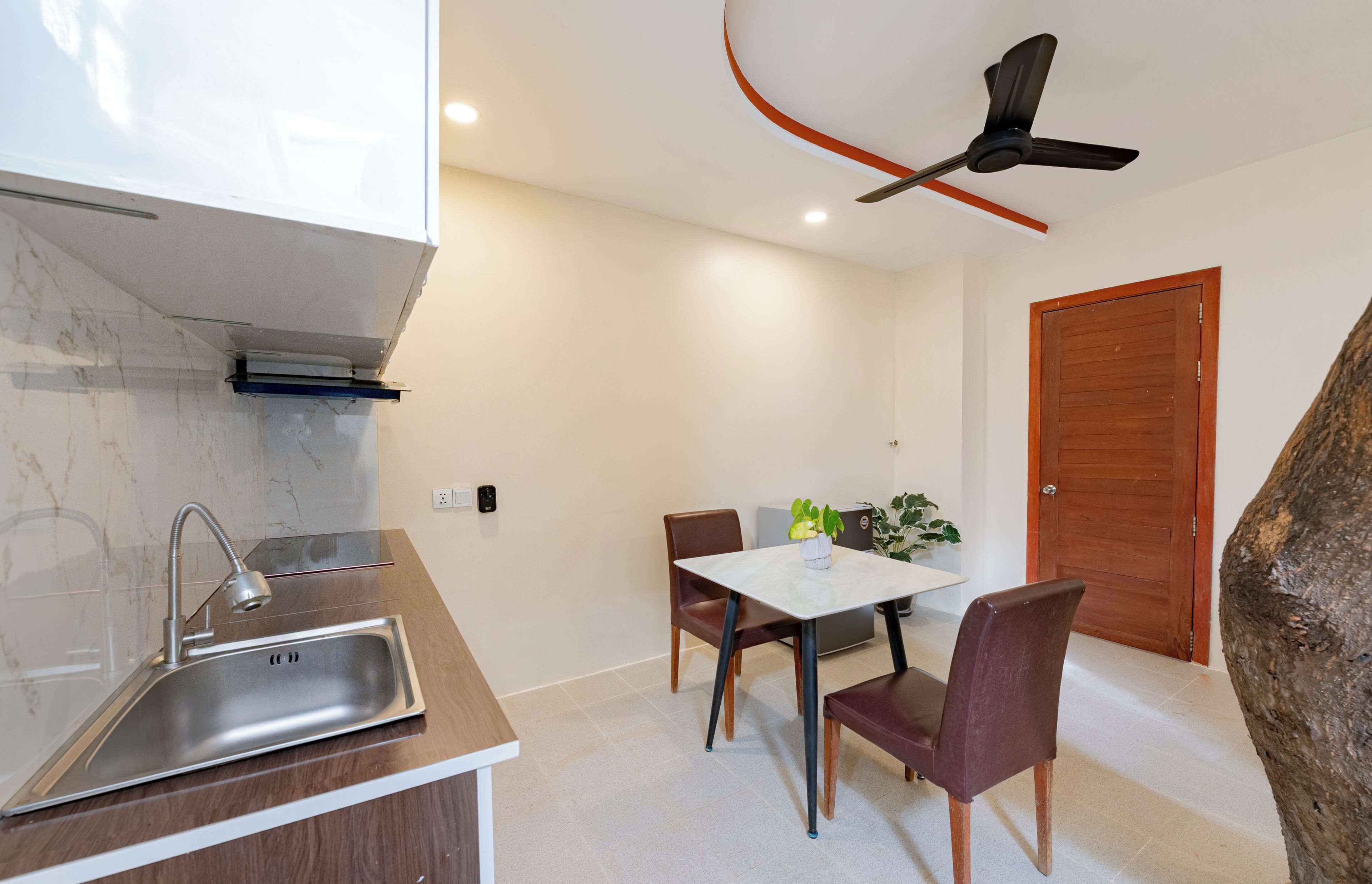 A modern kitchen with a sink, dining table, chairs, and a ceiling fan.