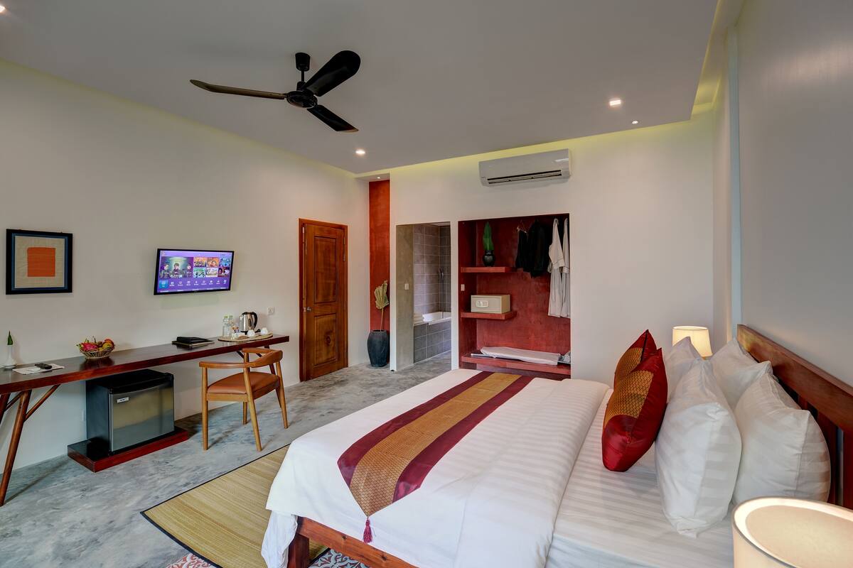 A hotel room with a bed, desk, chair, television, and a ceiling fan.