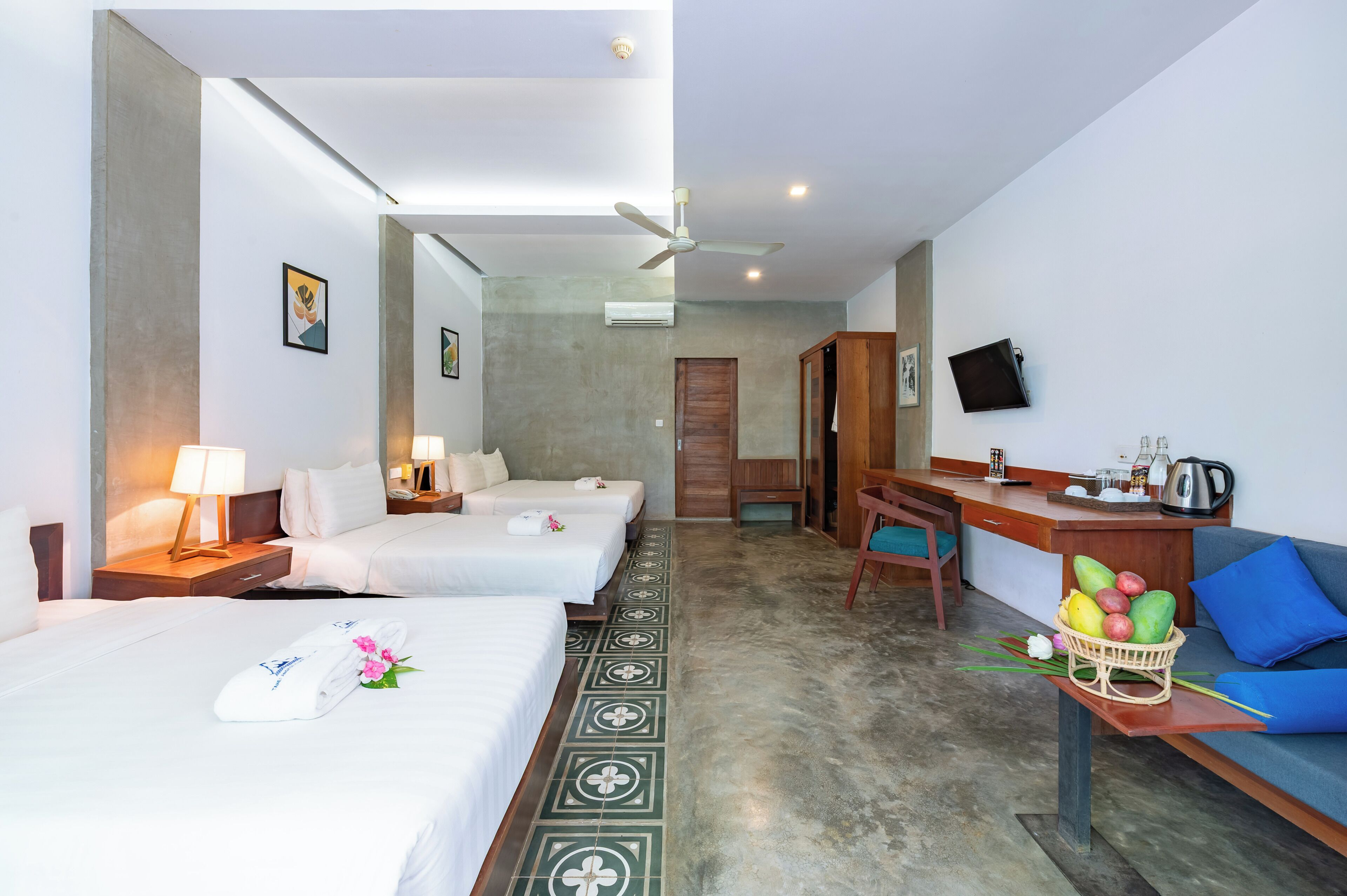 A hotel room with two beds, a desk, a chair, a television, and a fruit basket.