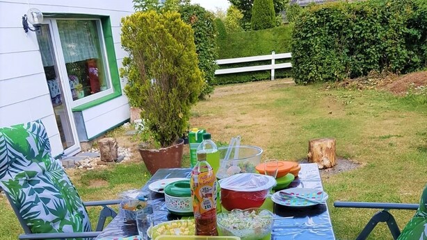 An outdoor dining table set up with various food items and drinks, surrounded by chairs and a house in the background. - Pension Falter (Nideggen)