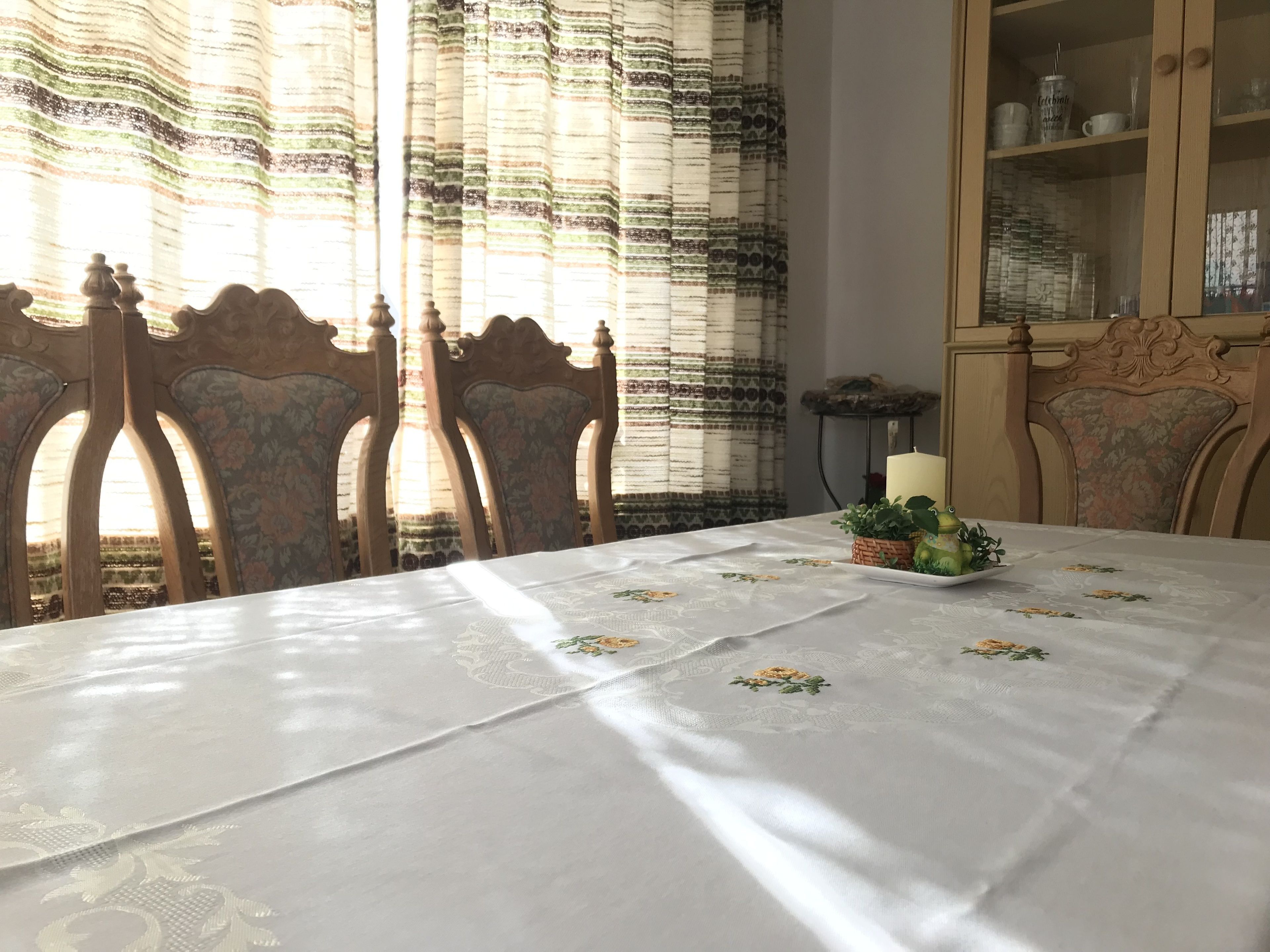 A dining area with a table covered by a white tablecloth, wooden chairs, a candle, and a small plant on the table.