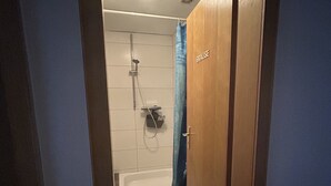 A narrow hallway leading to a bathroom with a shower, a bathtub, and a towel rack. - Pension Falter (Nideggen)