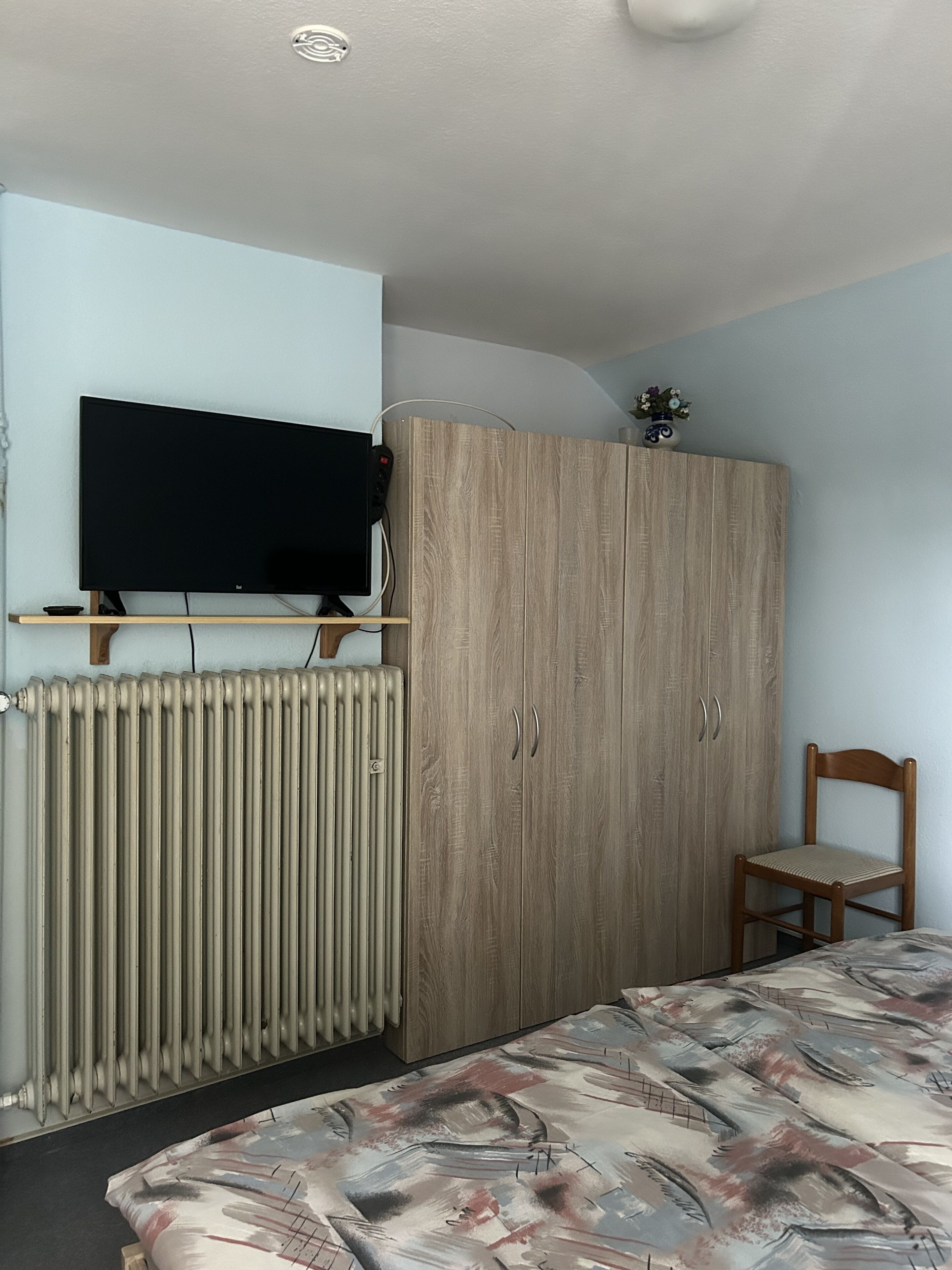 Ein Schlafzimmer mit einem Bett, einem Holzschrank, einem an der Wand montierten Fernseher und einer Heizung.