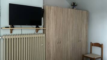 Ein Schlafzimmer mit einem Bett, einem Holzschrank, einem an der Wand montierten Fernseher und einer Heizung.