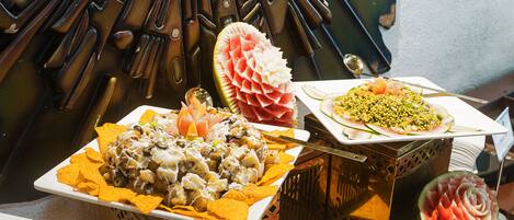Buffet com nachos, uma melancia esculpida em flor e um prato de salada.