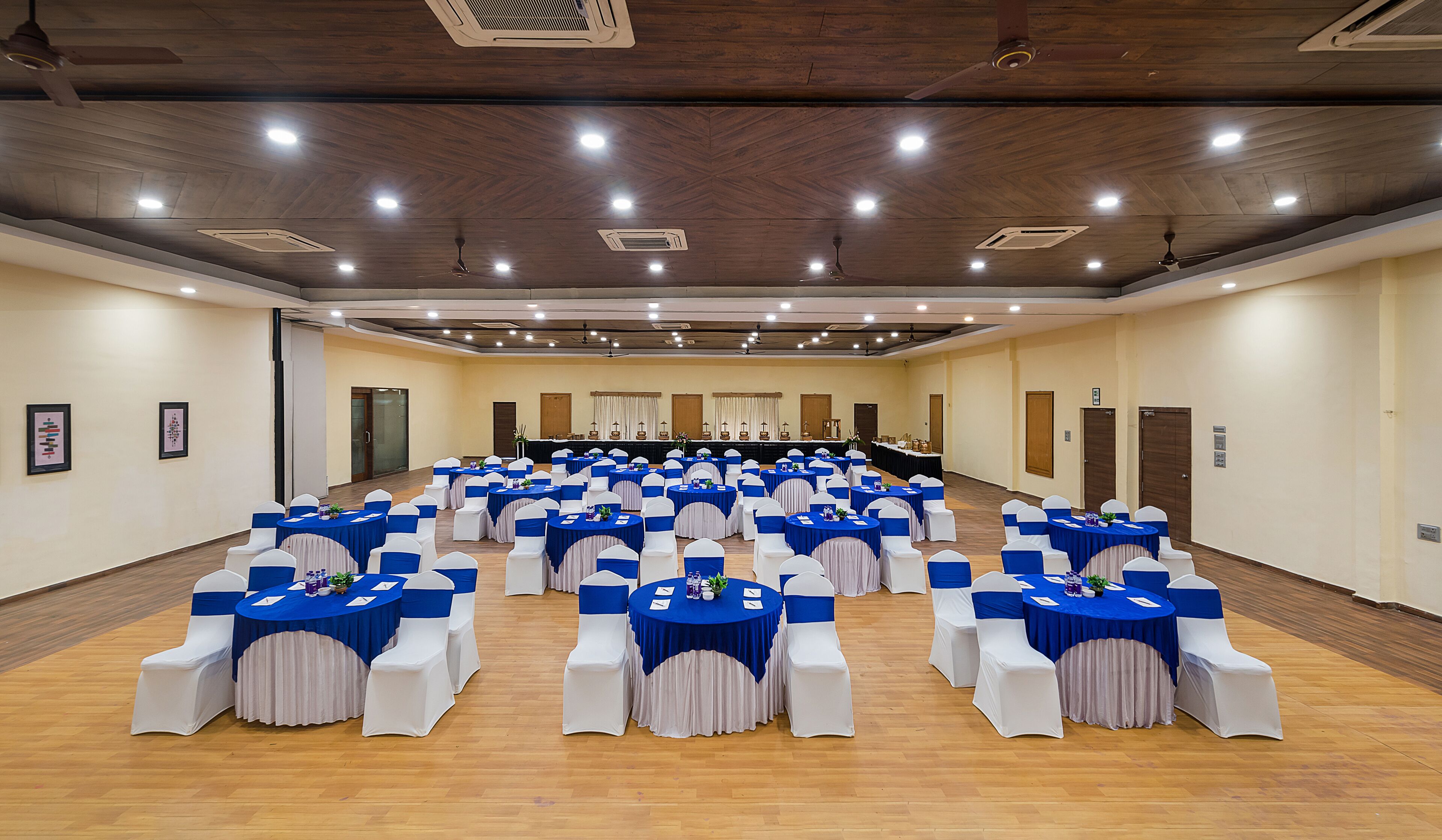 Une grande salle de conférence, dotée de rangées de tables et de chaises, et équipée de luminaires au plafond et d’un système de ventilation.