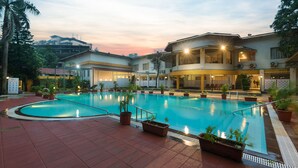 A swimming pool with surrounding potted plants, a covered seating area, and a building with multiple floors and balconies. - Manas Lifestyle Resort Igatpuri (Igatpuri)
