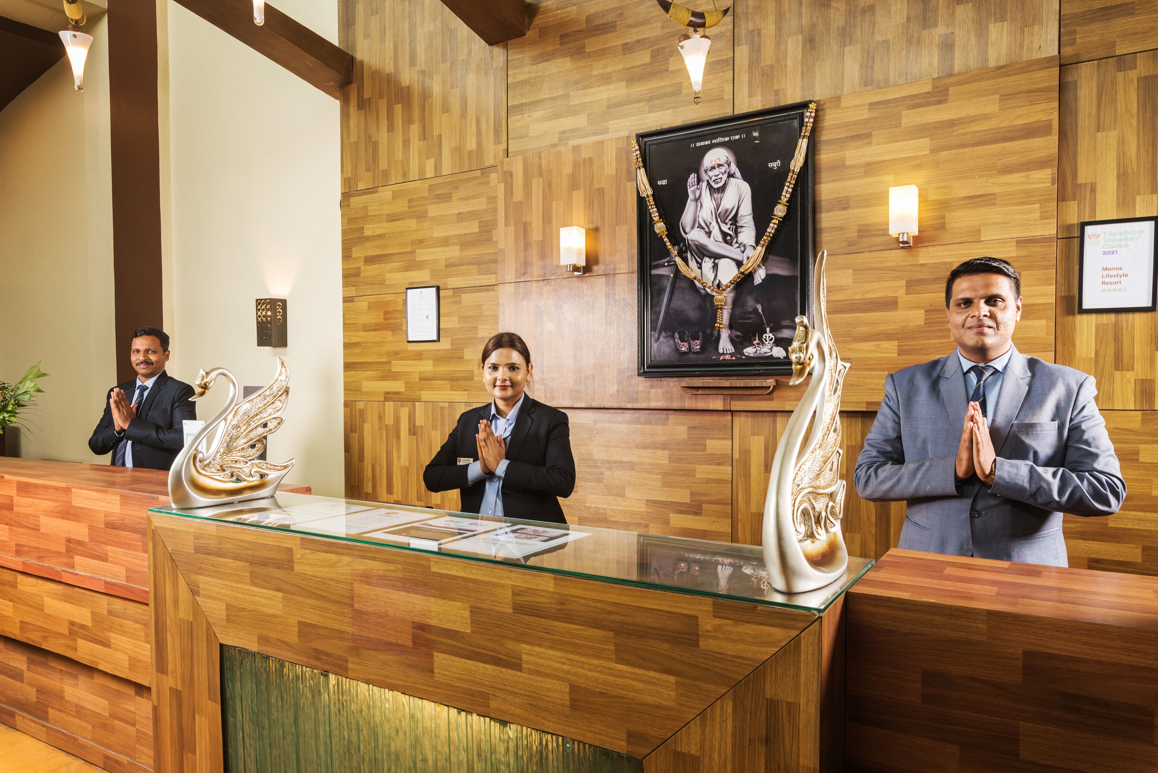 A reception desk with three staff members standing behind it, wooden paneling on the walls, and a framed picture above the desk.