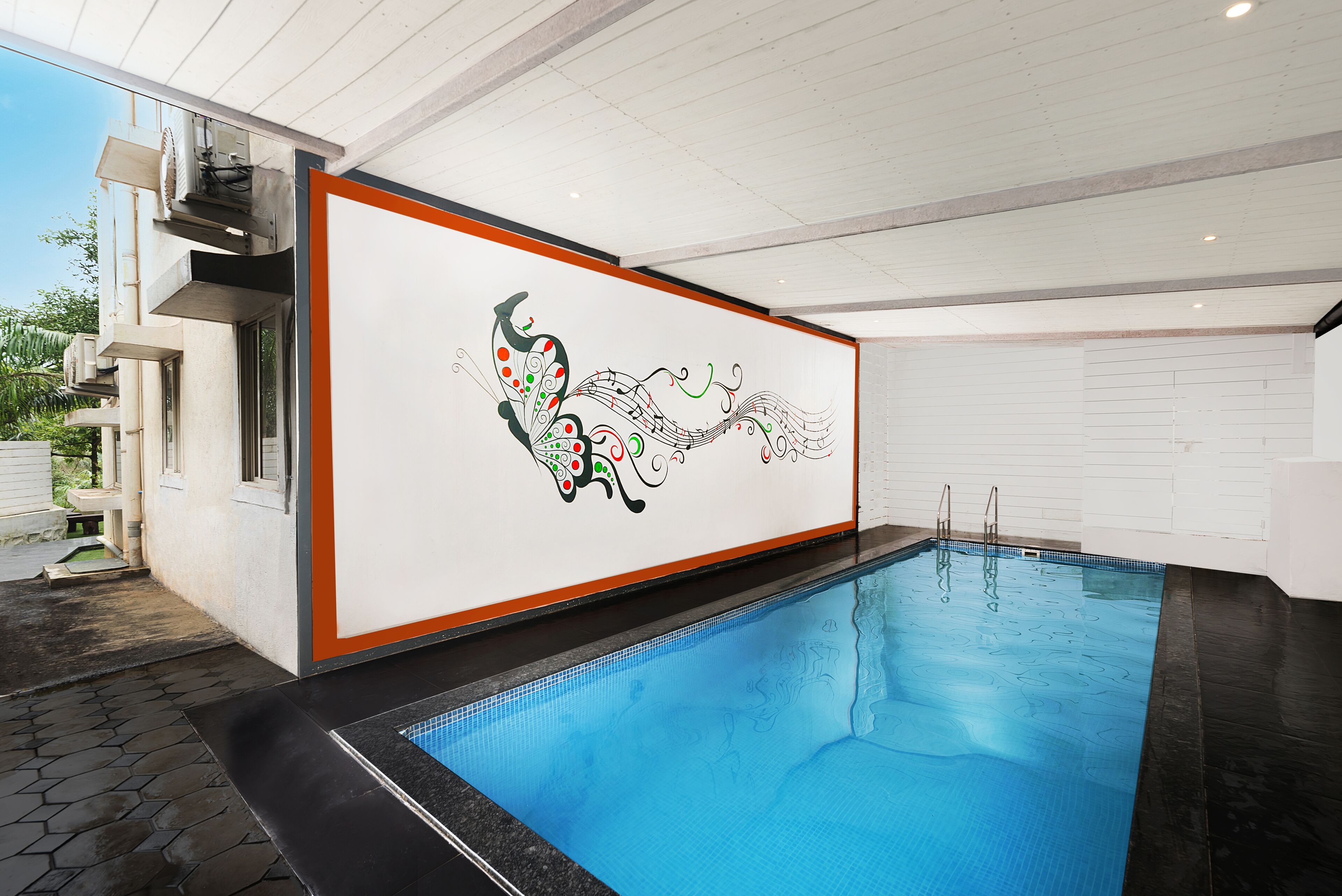 An indoor swimming pool with a decorative wall mural, a clear pool edge, and a tiled floor.