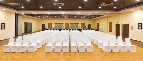 Un salón de conferencias con filas de sillas blancas, una mesa larga, suelo de madera y una alfombra estampada en patrón de rombos.