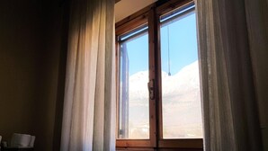 Une pièce avec une fenêtre donnant sur un paysage montagneux, un radiateur situé sous la fenêtre et un petit meuble sur le côté gauche.