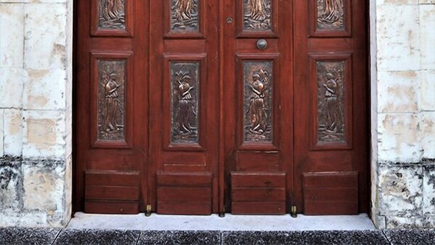 Una puerta doble de madera con intrincados detalles de metal y un muro de piedra.