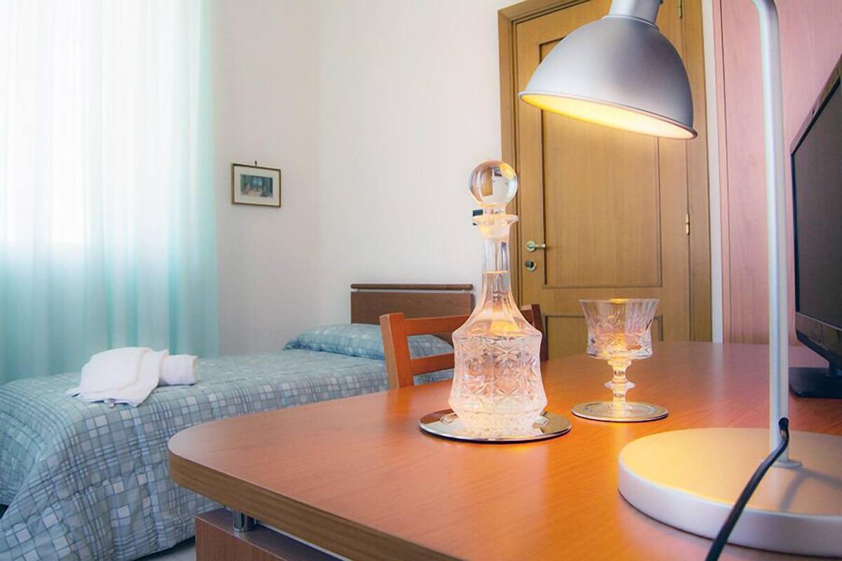 A hotel room with a wooden table, a lamp, a crystal decanter, and a glass candle holder.