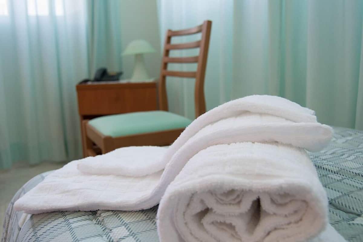 A neatly made bed with rolled white towels and a wooden nightstand with a lamp.