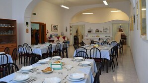Un comedor con varias mesas y sillas, una cocina al fondo y una estantería con diversos objetos.