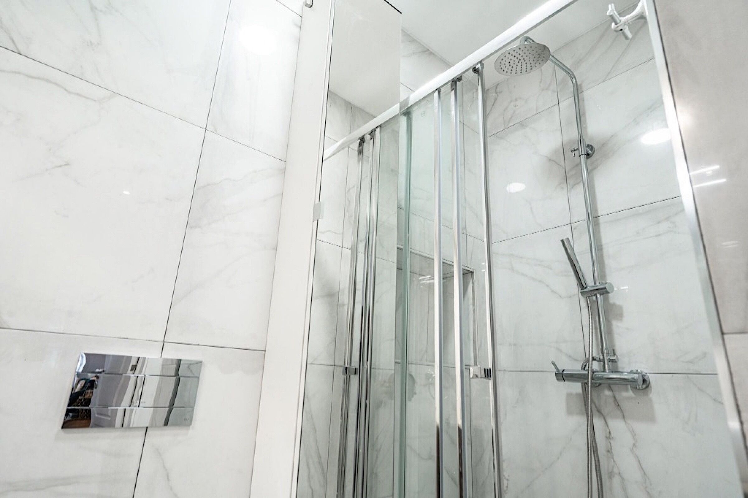 A modern bathroom with a glass-enclosed shower, marble tiles, and a built-in vanity.