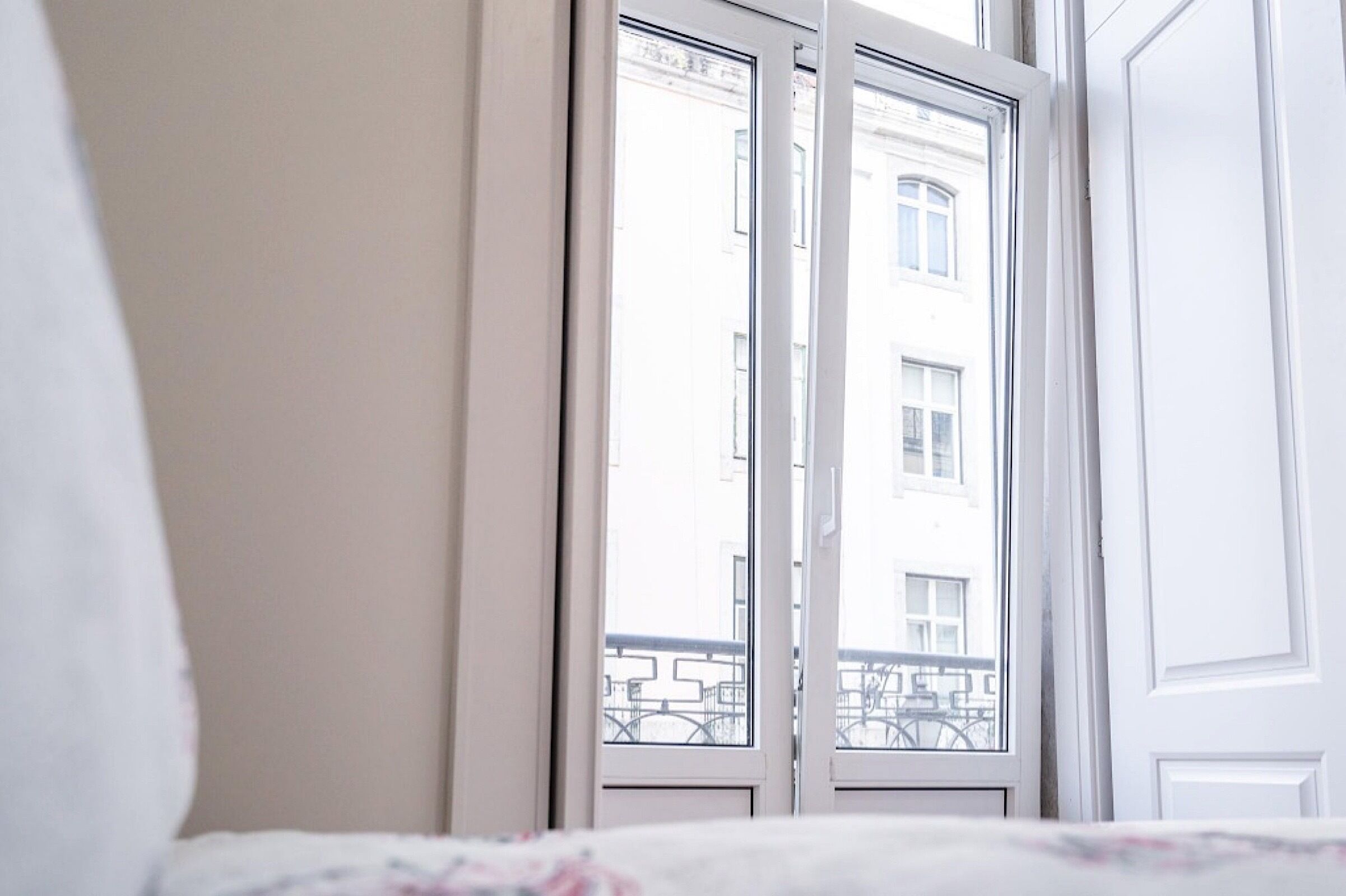 A hotel room with a large window, a bed with a floral bedspread, and a white door.