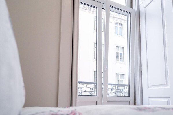 A hotel room with a large window, a bed with a floral bedspread, and a white door.