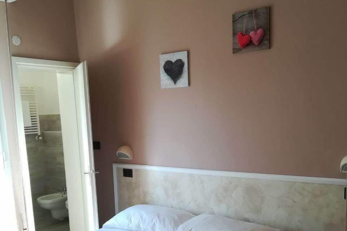 A bedroom with a bed, a towel, a wall-mounted heart decoration, and a small bedside table.