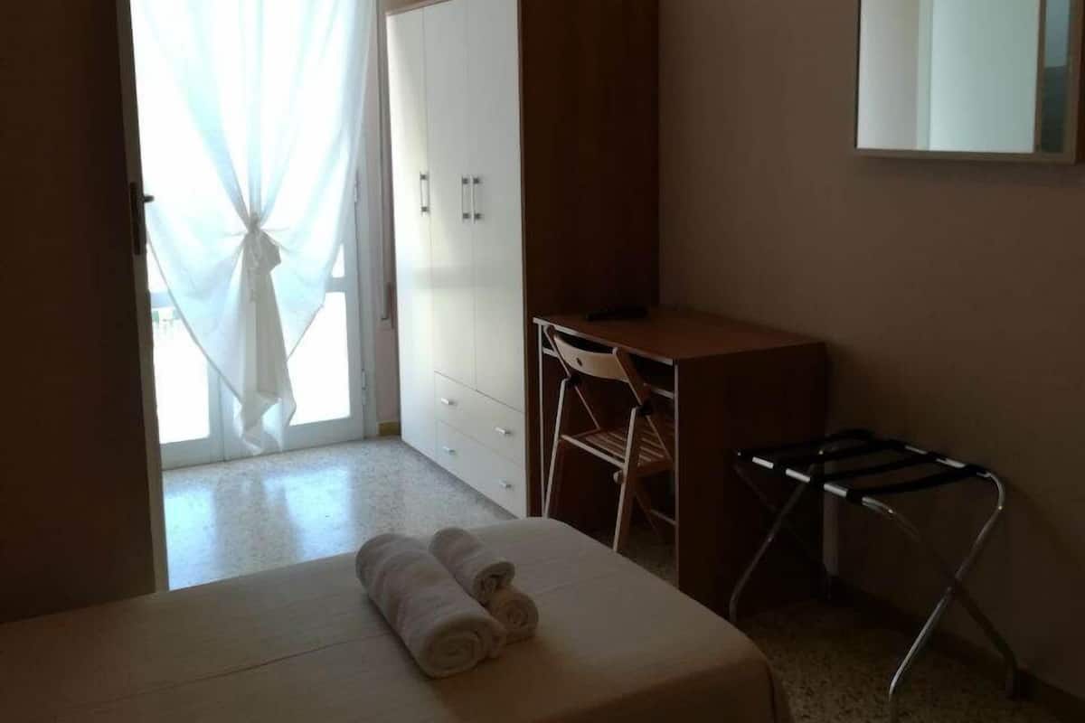 A hotel room with a bed, a desk, a wardrobe, and a mirror.