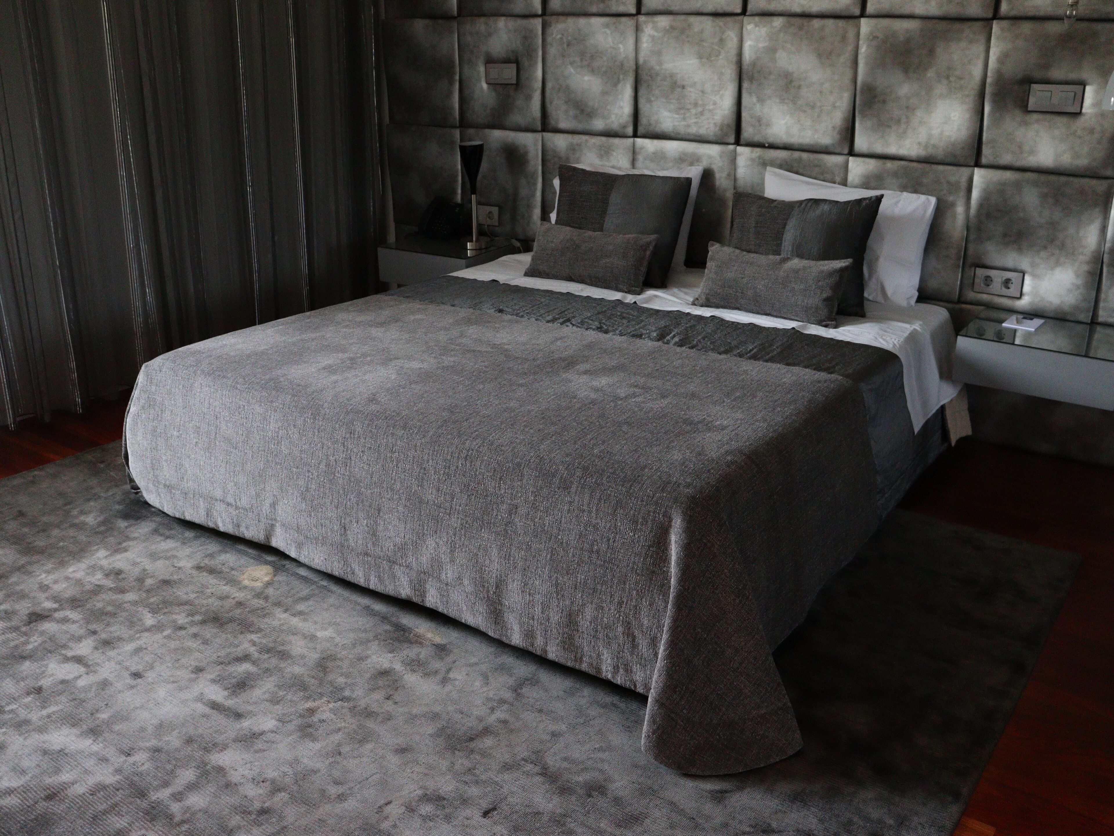 A modern bedroom with a large bed, grey bedding, and a tufted headboard.