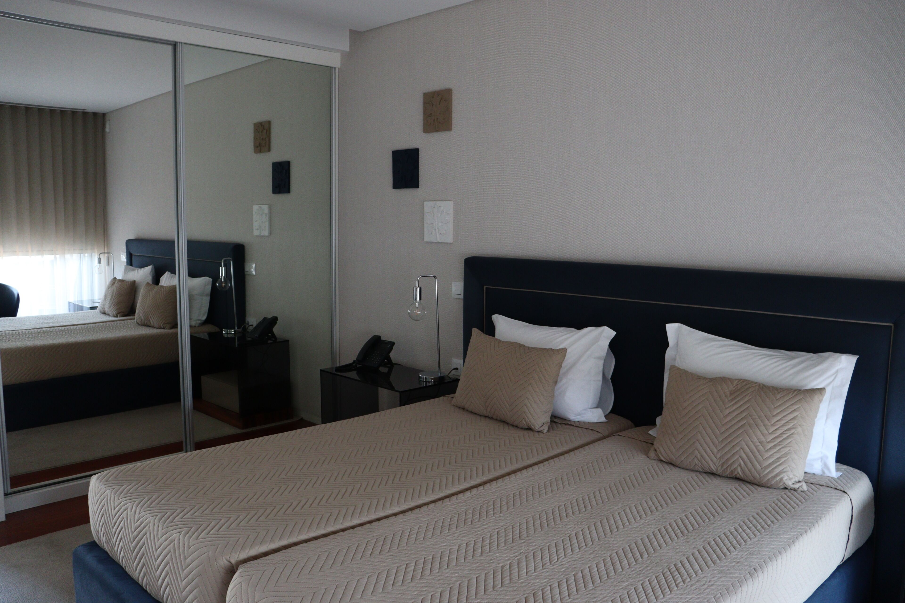 A hotel room with a large bed, a bedside table, a mirror, and a window with curtains.