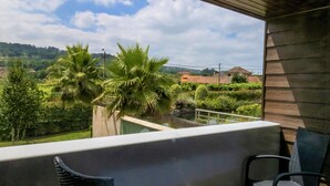 A balcony with two chairs and a small table, overlooking a lush landscape with palm trees and distant hills. - FH Hotel (Felgueiras)