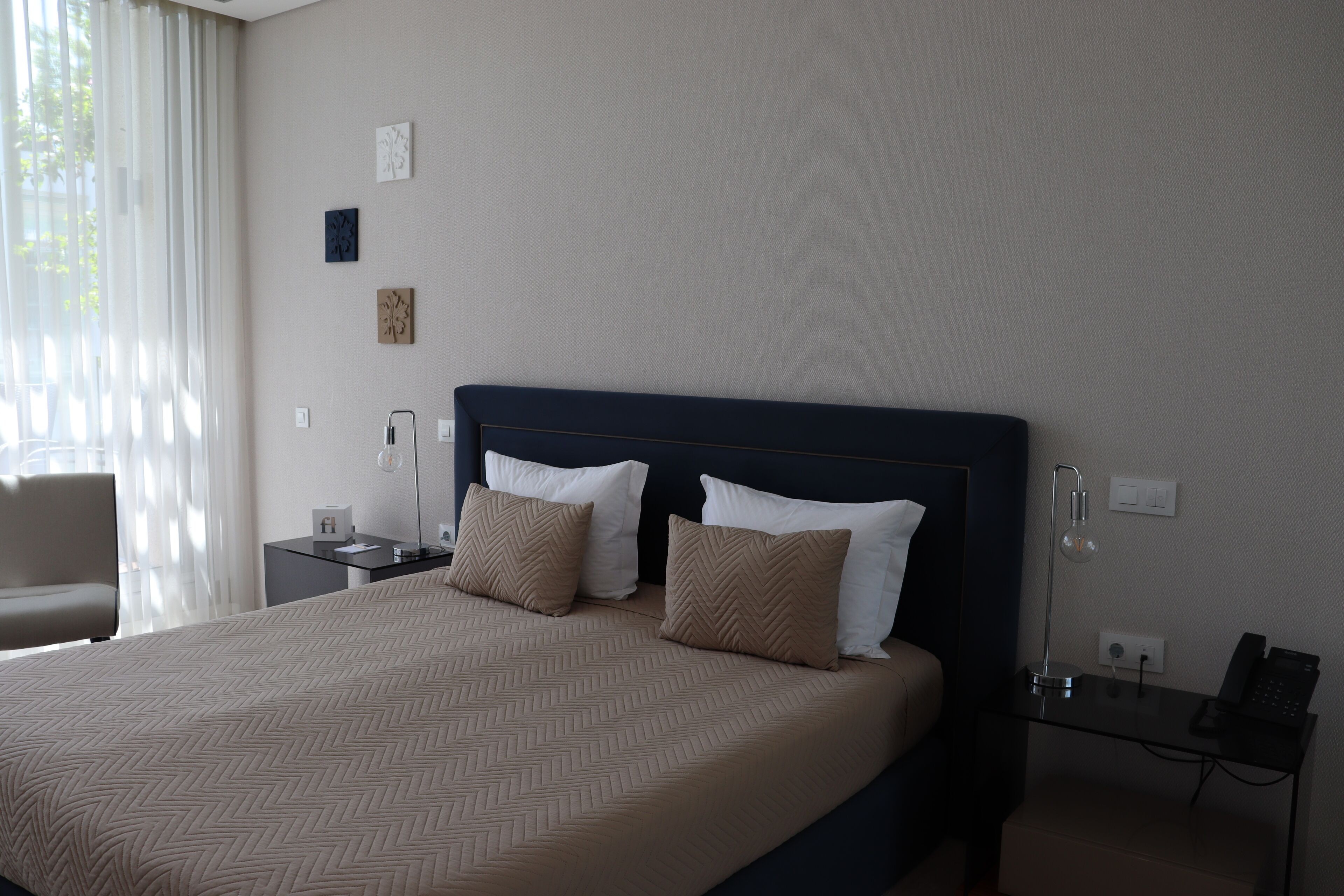 A hotel room with a large bed, two bedside tables, a chair, and a desk with a phone.