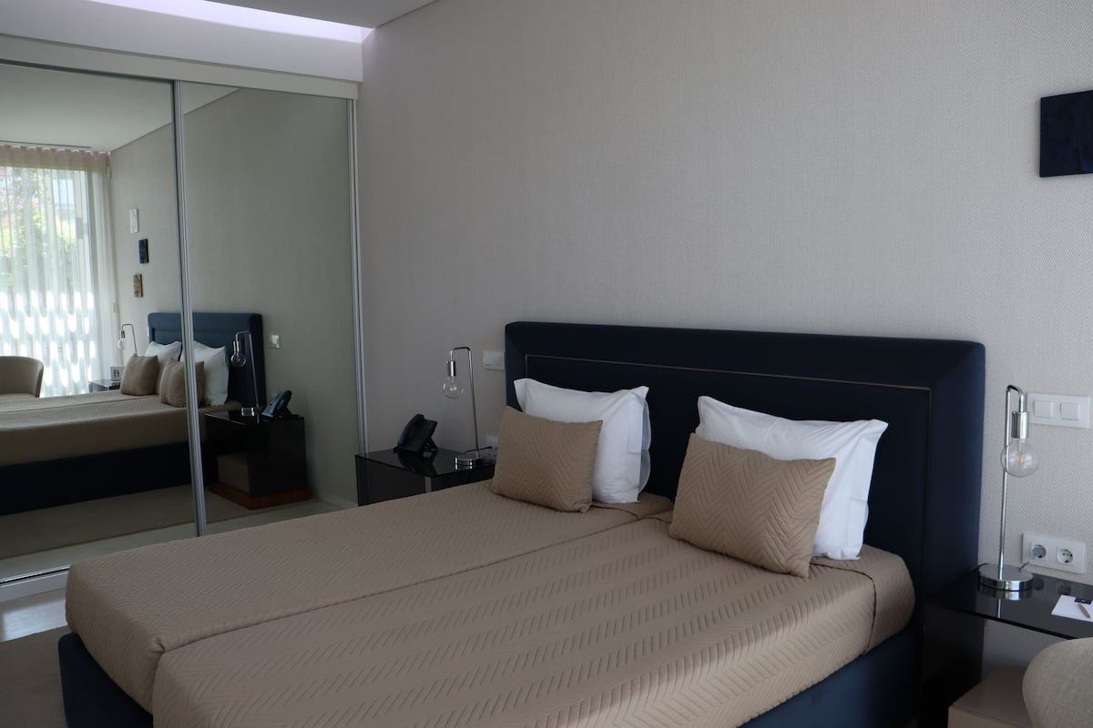A hotel room with a large bed, a bedside table with a lamp, and a mirror on the wall.