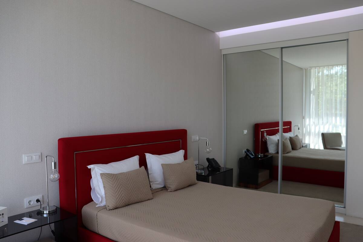 A modern hotel room with a large bed, a glass partition, and a red headboard.