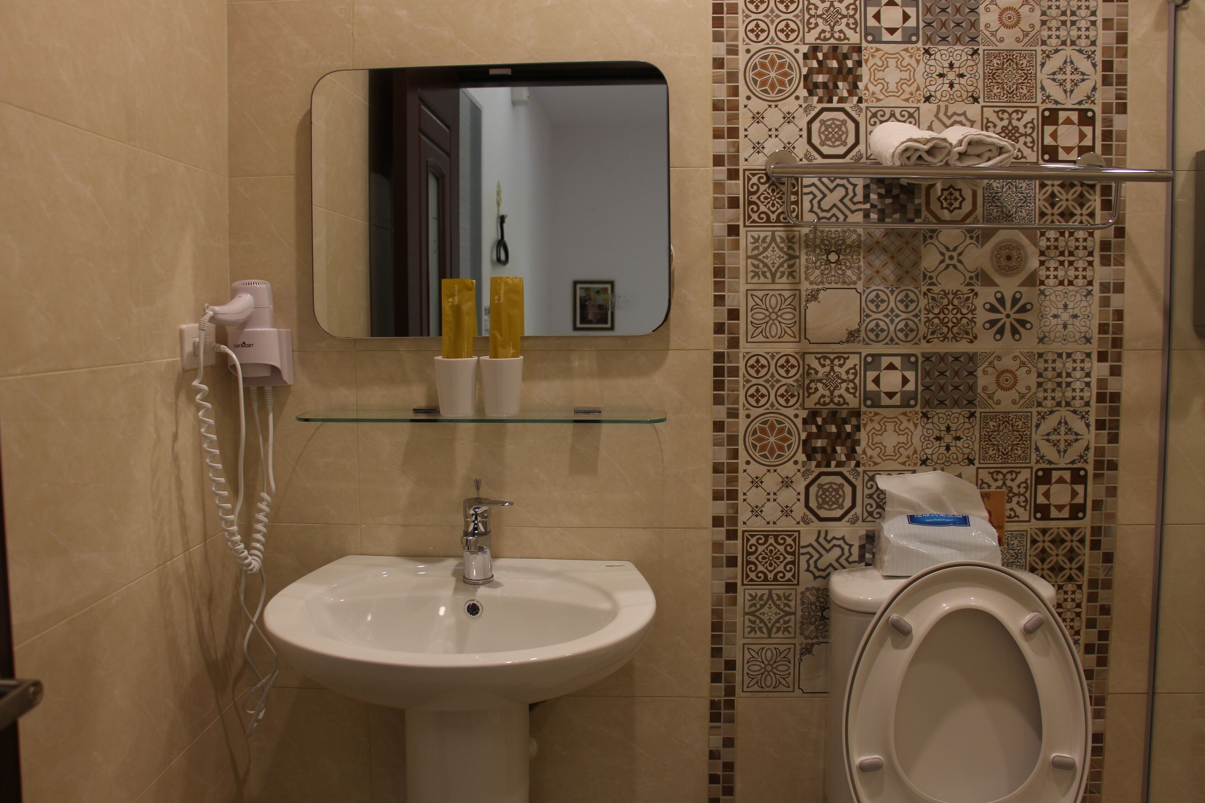 A bathroom with a sink, mirror, and toilet. There are toiletries on the wall and a towel rack.