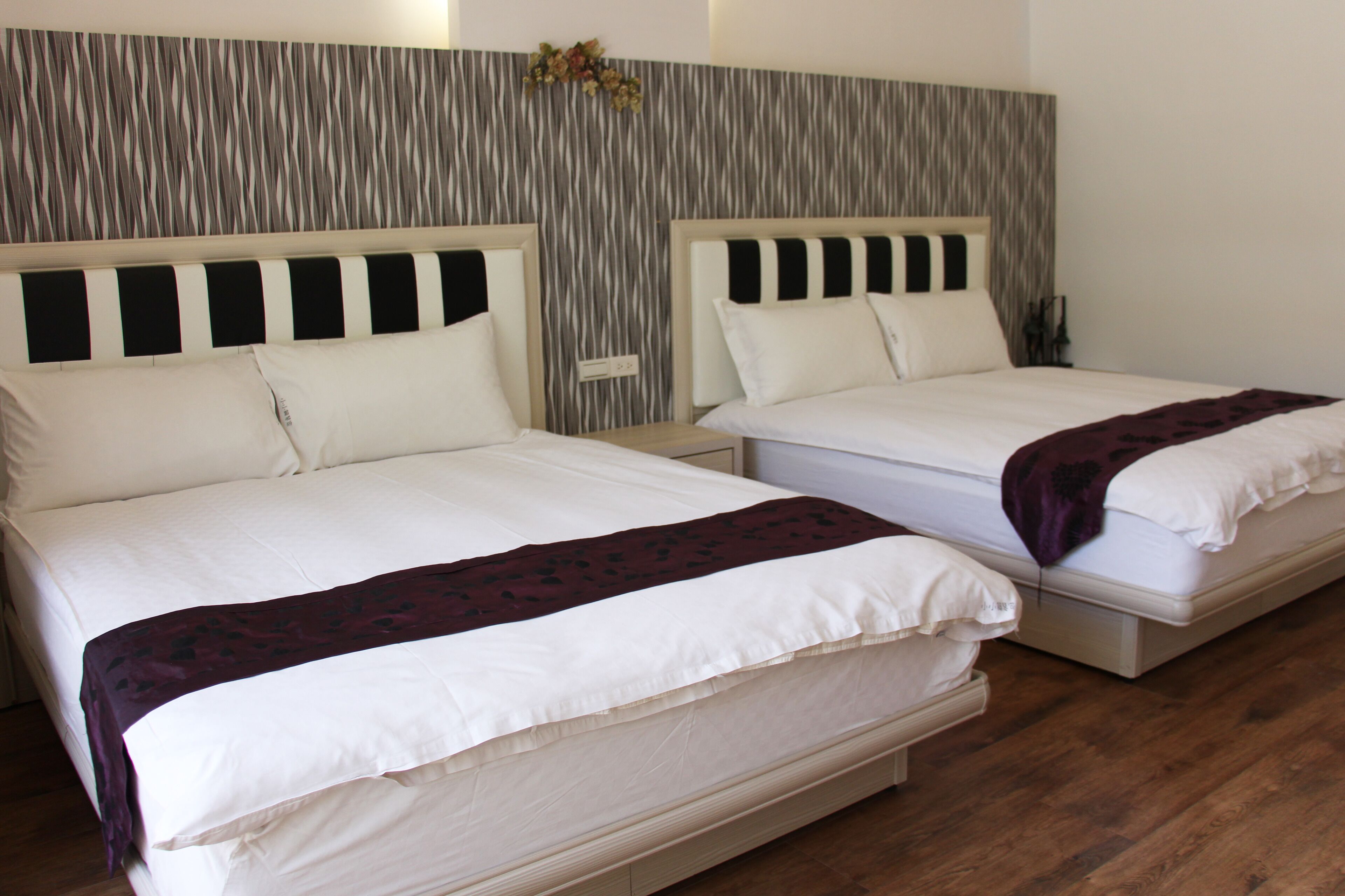 Two single beds with white bedding and headboards, a wooden floor, and a textured wall behind the beds.