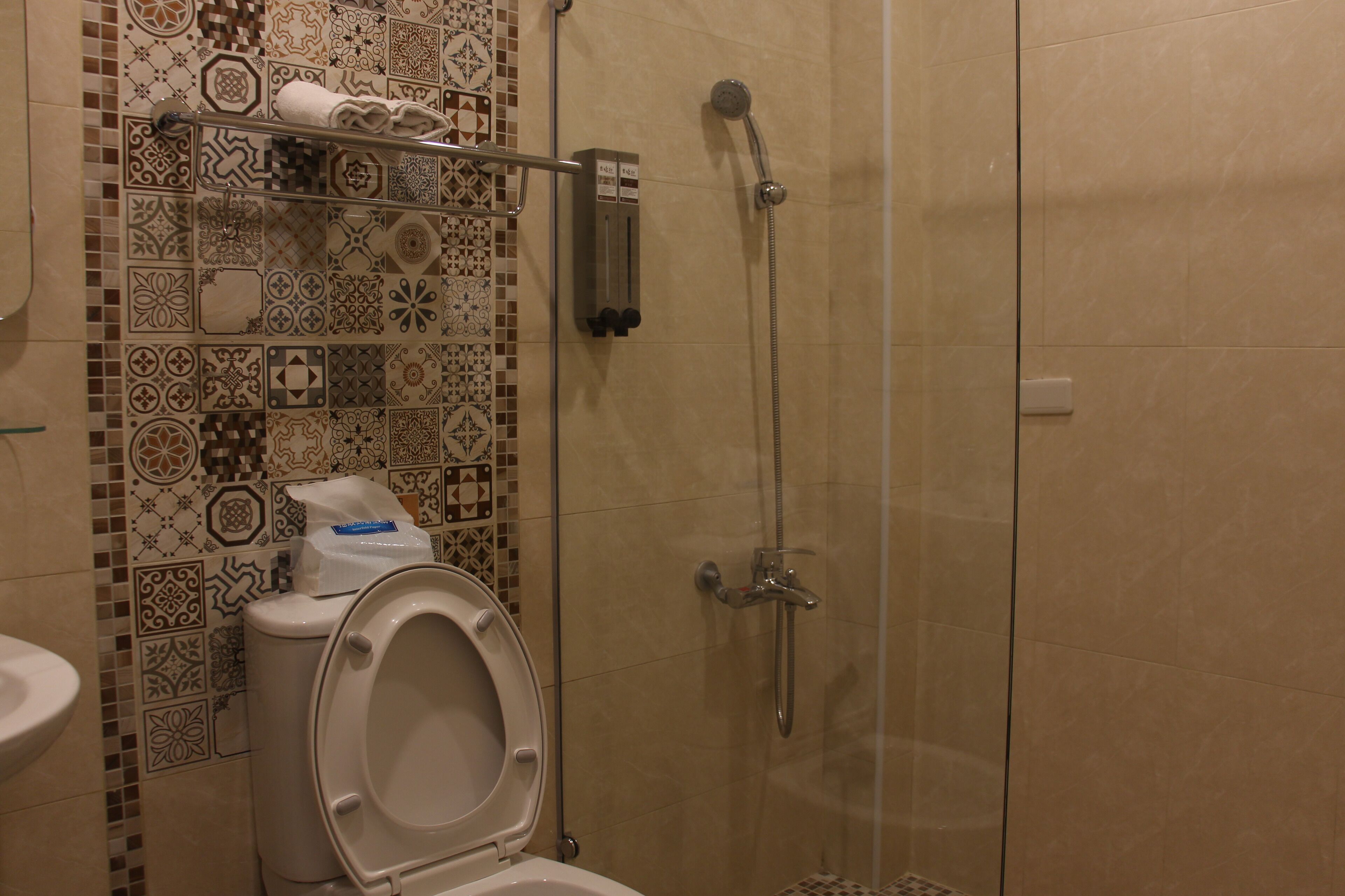 A bathroom with a toilet, a shower, and a tiled wall.