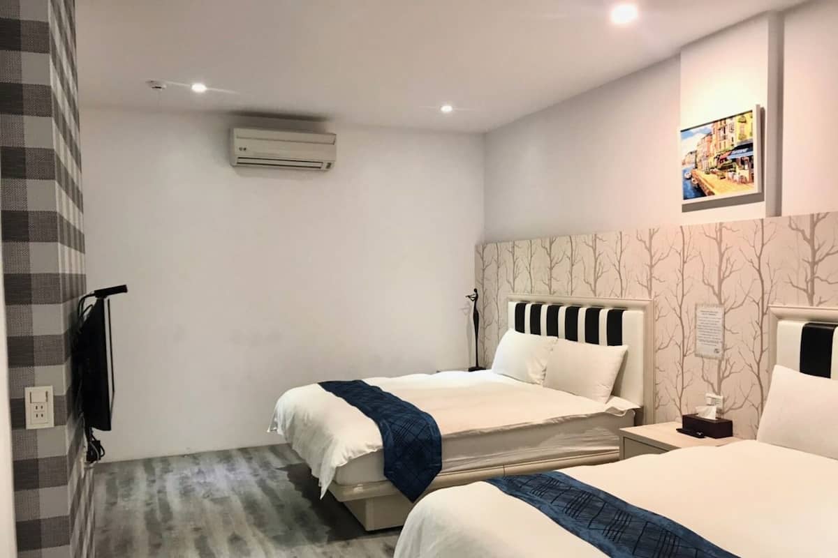A hotel room with two beds, a ceiling fan, an air conditioning unit, a trash bin, and a wall-mounted picture.
