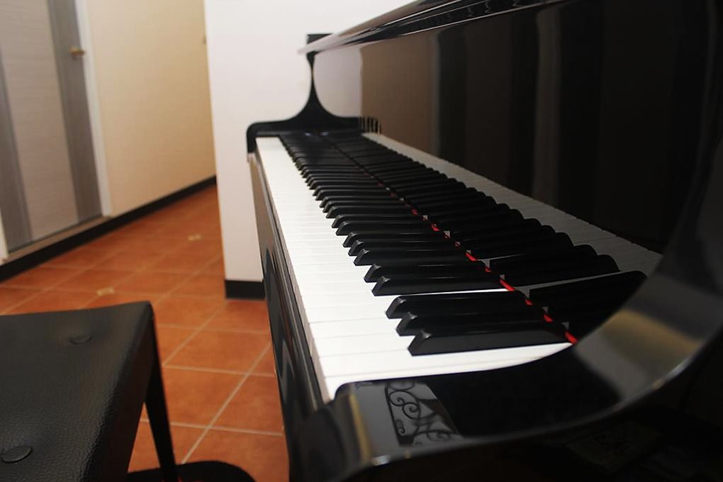 A piano with a black and white keyboard, a bench in front, and a tiled floor.