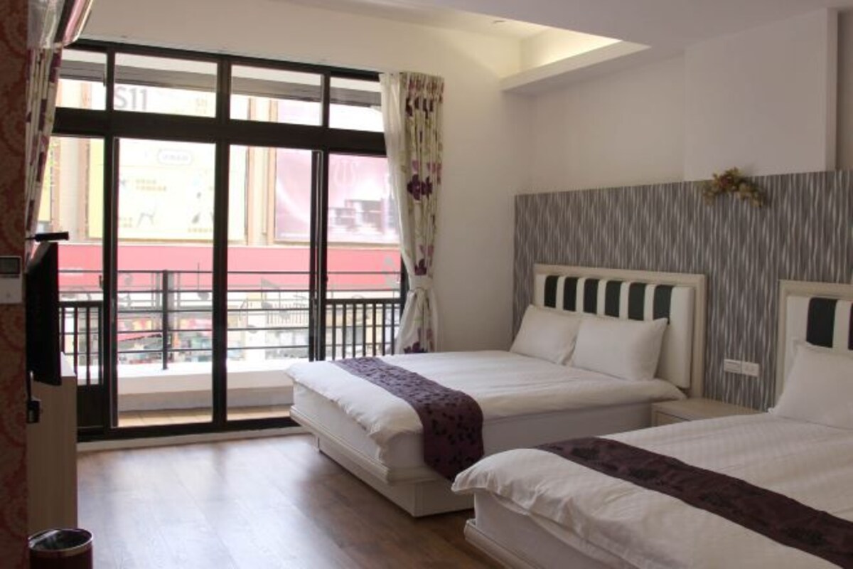 A hotel room with two beds, a balcony, and a view of the street.