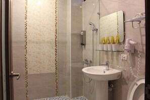 A bathroom with a glass shower enclosure, a sink with a mirror, and toiletries on the wall.