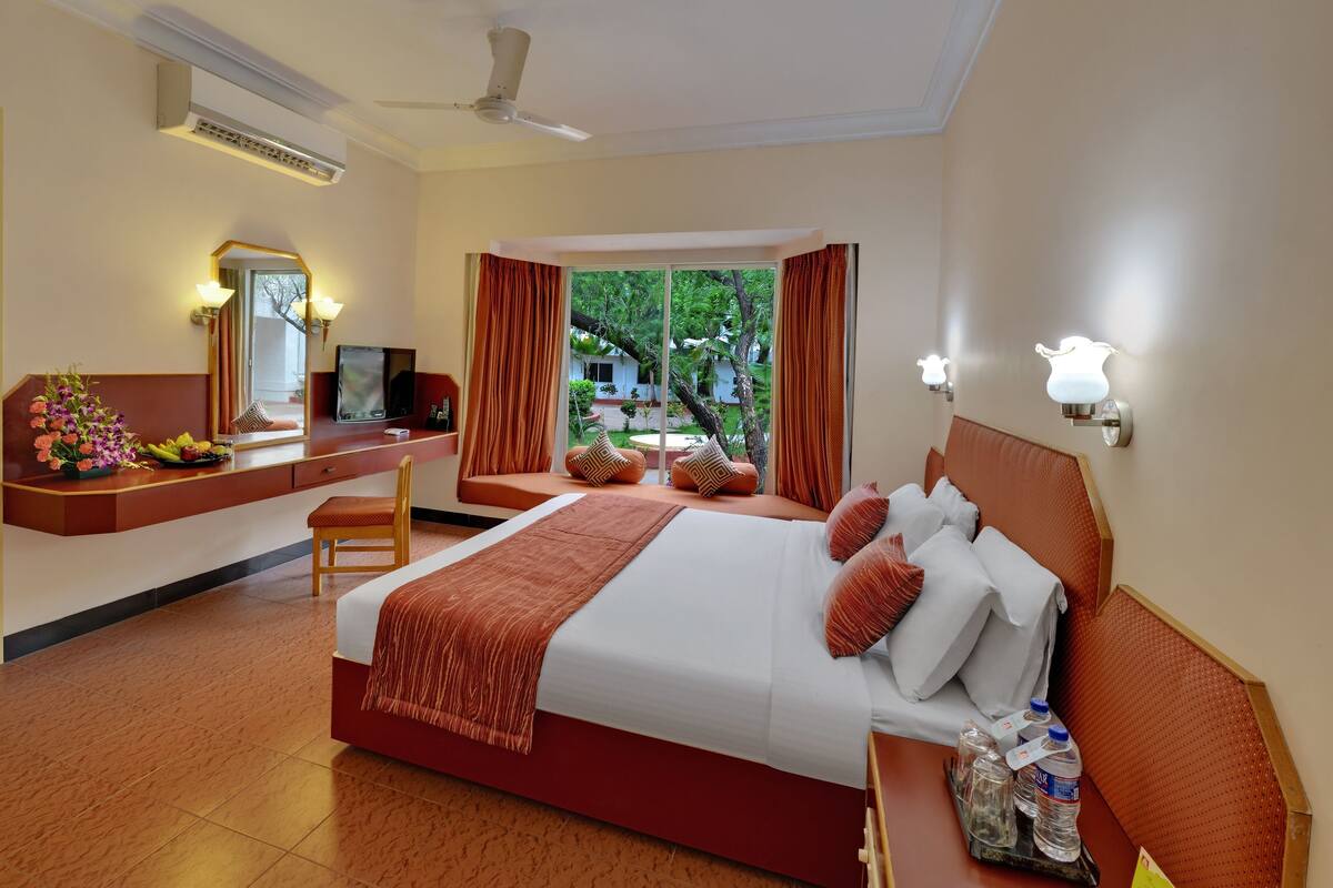 Ein Hotelzimmer mit Bett, Schreibtisch mit Stuhl, Spiegel und einem Fenster mit Vorhängen.