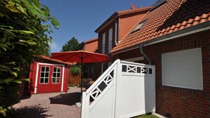 A brick house with a red door, a white gate, and a red umbrella. - No. 39 - Cottage At the marina (Wittmund)